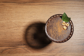 Dessert bowl of delicious hot chocolate with hazelnuts and fresh mint on wooden table, top view. Space for text