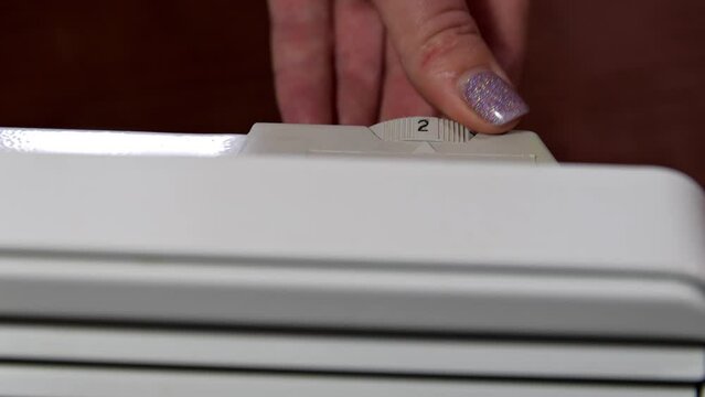 Close-up of a woman's hand switches the heater thermostat mode. A woman turns off an electric convector in order to save electricity. Cold temperature, energy crisis.