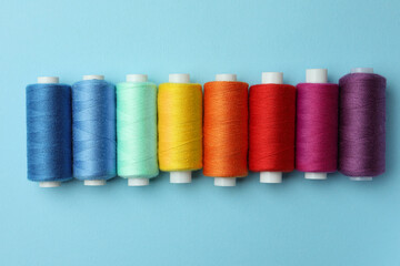 Set of different colorful sewing threads on light blue background, flat lay
