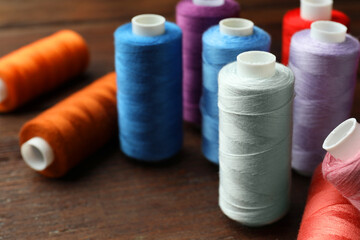 Different colorful sewing threads on wooden table, closeup