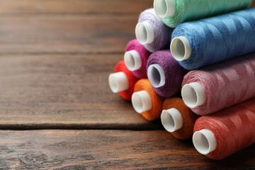Stack of colorful sewing threads on wooden table, closeup. Space for text