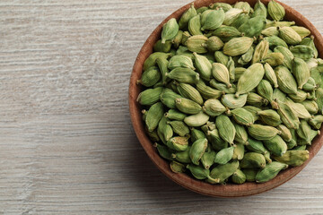 Bowl of dry cardamom pods on white wooden table, top view. Space for text