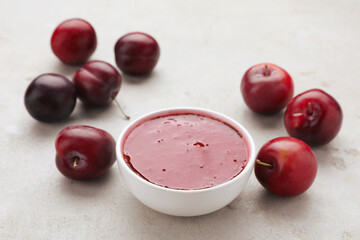 Plum puree in bowl and fresh fruits on light grey table