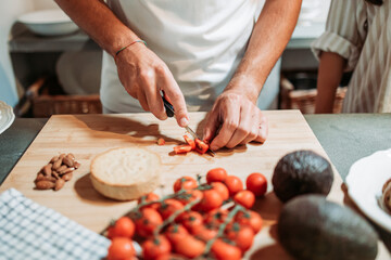 Male hands cutting cherry tomato on the kitchen board. Salad preparation.