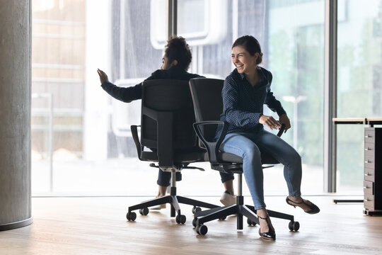 Cheerful Indian office employees, joyful colleagues have fun together at workplace, finish task successfully, enjoy break, workday end, riding seated on chairs looking overjoyed celebrate work result - Powered by Adobe