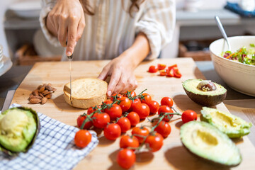 Female hands cutting slices of almond vegan cheese for breakfast