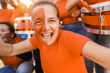 Orange sport fans screaming while supporting their team - Football supporters having fun at...