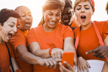 Orange sport supporters watching football game on mobile phone - Focus on center woman face -...
