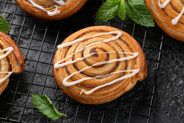Freshly baked sweet cinnamon swirls with icing on cooling rack. Sweet food