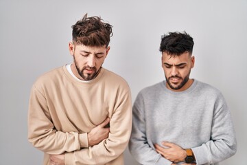 Young homosexual couple standing over white background with hand on stomach because indigestion, painful illness feeling unwell. ache concept.