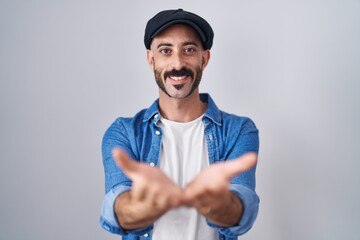 Hispanic man with beard standing over isolated background smiling with hands palms together...