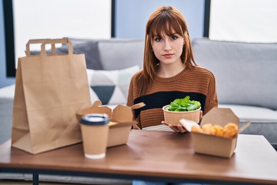 Young Beautiful Woman Eating Delivery Food At The Living Room Thinking Attitude And Sober Expression Looking Self Confident