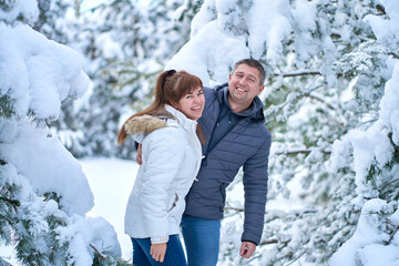 Fototapeta na wymiar A joyful couple in love walking in winter forest heavy covered with snow