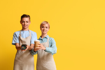 Young baristas with payment terminal and cup of coffee on yellow background