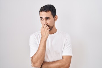 Handsome hispanic man standing over white background looking stressed and nervous with hands on mouth biting nails. anxiety problem.