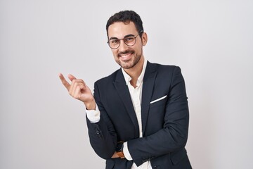 Handsome business hispanic man standing over white background with a big smile on face, pointing with hand finger to the side looking at the camera.