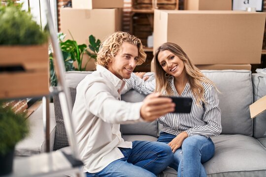 Man and woman couple make selfie by the smartphone sitting on sofa at new home