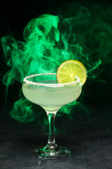 Glass of tasty margarita cocktail with smoke on dark color background