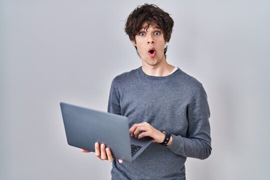 Young man working using computer laptop scared and amazed with open mouth for surprise, disbelief face
