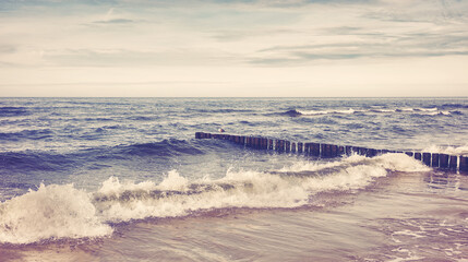 Retro toned picture of an empty beach with crashing wave.