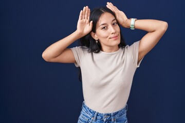 Young hispanic woman standing over blue background doing bunny ears gesture with hands palms...