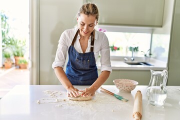 Young blonde woman smiling confident make pizza dough with hands at kitchen