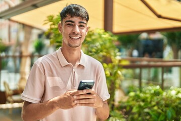 Young hispanic man smiling confident using smartphone at street