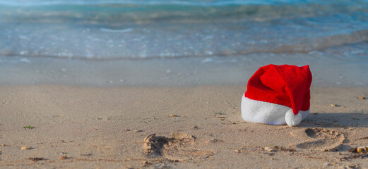 Hat and footprints on the sand of Santa Claus on the beach. Santa went swimming and cool off in the sea during the holidays. Celebrate Christmas and New Year while traveling to warm countries.  banner