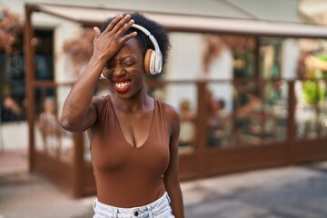 African woman with curly hair outdoors at the city wearing headphones clueless and confused...