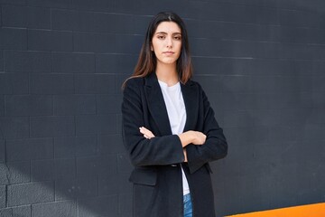 Young beautiful hispanic woman standing with serious expression and arms crossed gesture over isolated black background