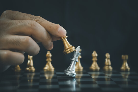Businessman hand moving gold chess king figure and checkmate opponent during chessboard competition. Decision achievement goal, success, management, business planning, disruption and leadership.