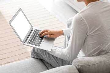 Young man using laptop on sofa at home, closeup