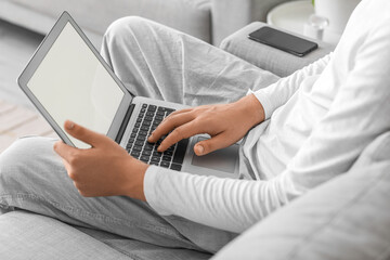 Fototapeta premium Young man using laptop on sofa at home, closeup