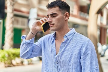 Young hispanic man talking on the smartphone with serious expression at street