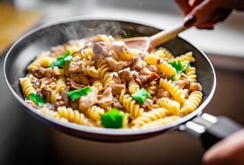 woman hand cooking tasty chicken fillet with mushroom in a creamy sauce with fusilli pasta in pan on kitchen