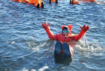 A woman in sunglasses raised both arms swimming in cold ice water pond with orange color of water right thermal suit, tourist adventure activity, Arctic Circle