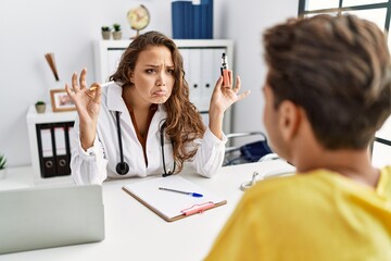 Obraz premium Young doctor woman showing electronic cigarette and normal cigarrete to patient depressed and worry for distress, crying angry and afraid. sad expression.