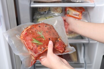 Woman putting vacuum bag with meat into fridge, closeup. Food storage