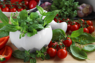 Mortar with fresh herbs, pepper and cherry tomatoes on wooden table, closeup