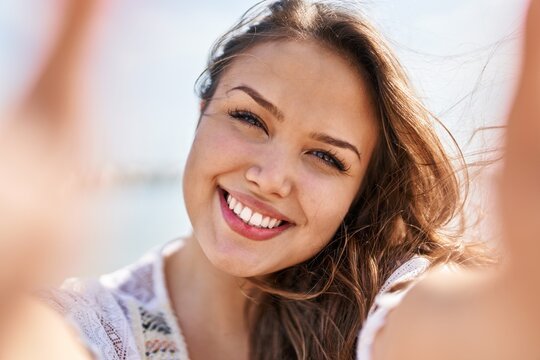 Young beautiful hispanic woman smiling confident making selfie by the smartphone at beach
