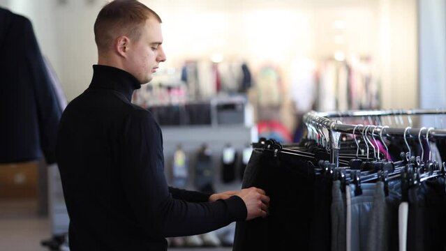 Camera follows the man in clothing store. Male try to fing some new clothes for autumn and winter. Hmansome customer in black golf