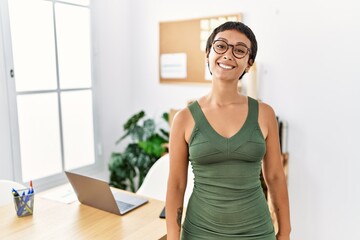 Young hispanic woman with short hair working at the office looking positive and happy standing and smiling with a confident smile showing teeth