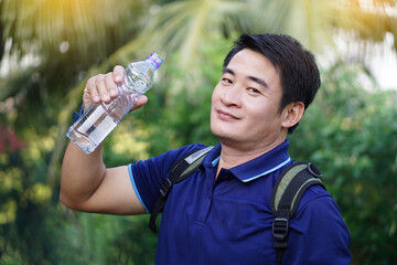 Handsome Asian man traveler holds bottle of drinking water to drink outdoors. Concept : Drinking water for health, Healthy lifestyle.Quenching thirst,reduce fatigue, refreshes body. 