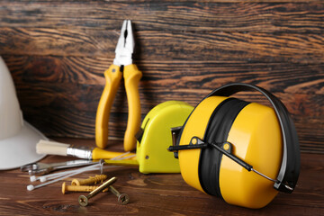 Hearing protectors with builder's tools on dark wooden background, closeup