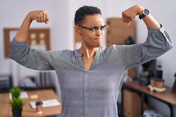 African american woman working at the office wearing glasses showing arms muscles smiling proud....
