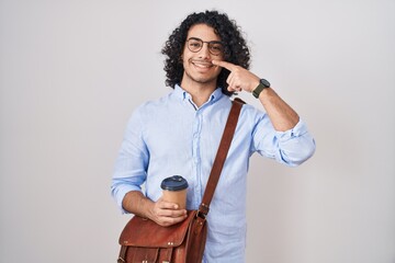 Hispanic man with curly hair drinking a cup of take away coffee pointing with hand finger to face and nose, smiling cheerful. beauty concept