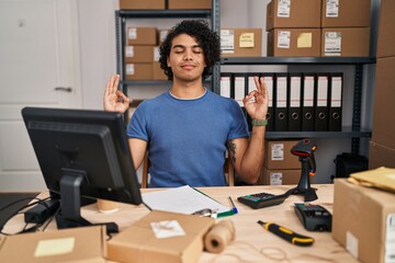 Hispanic man with curly hair working at small business ecommerce relaxed and smiling with eyes closed doing meditation gesture with fingers. yoga concept.