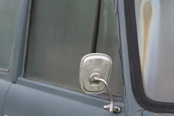 Selective focus shot of side mirror of grayish-blue abandoned van with dirty windows