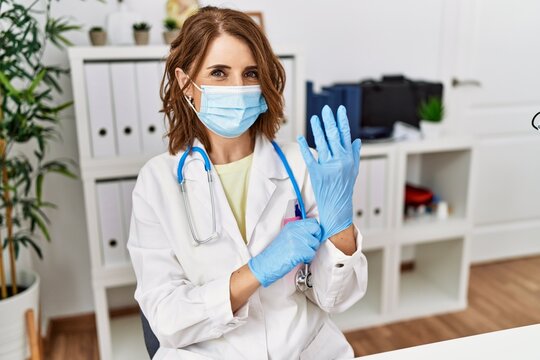 Middle age hispanic woman wearing doctor uniform and medical mask at clinic