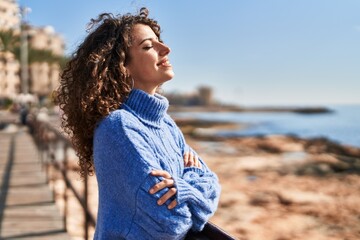 Young hispanic woman smiling confident breathing with arms crossed gesture at seaside
